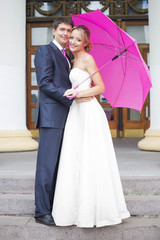 Young couple hugs in wedding gown with pink umbrella
