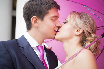 Young couple hugs in wedding gown with pink umbrella