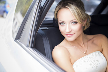 Fototapeta na wymiar Beautiful blonde bride in wedding gown sitting in a white car