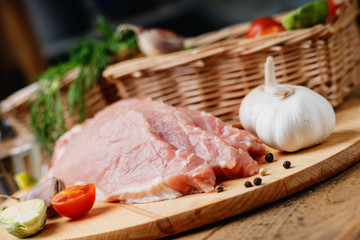Slices of raw pork meat and wicker basket with vegetables 