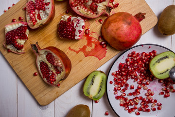 sliced fruit red pomegranate and kiwi on a cutting Board, a plate on white wooden background with knives close-up
