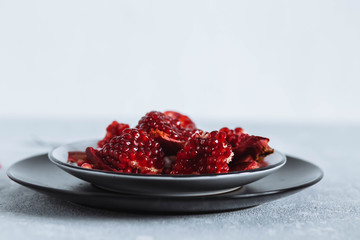 chunks of ripe red pomegranate in a white bowl on a light grey background rough table close-up copyspace