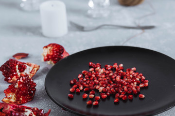 pieces and pomegranate seeds in black bowl on a gray white background around with a knife close-up top view
