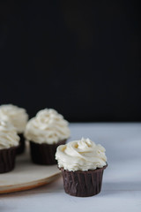 chocolate cupcakes white cream beige ceramic plate on white wooden table on black background close-up
