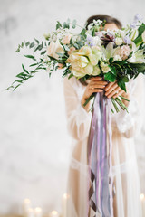 beautiful bride in white boudoir dress stands holding a bouquet covering her face in Studio on white background