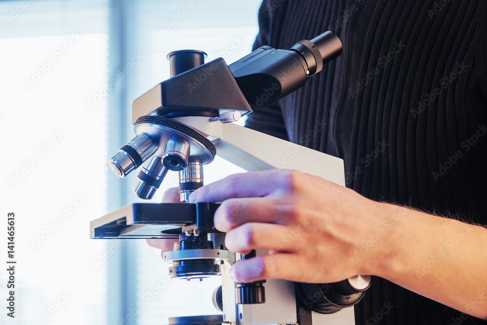 Poster close-up of scientist hands with microscope, examining samples.
