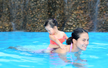 Pretty little girl with her mother in swimming pool outdoors