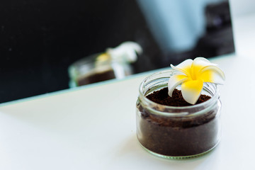 chocolate coconut coffee scrub in a glass jar with a flower near the mirror close-up copyspace
