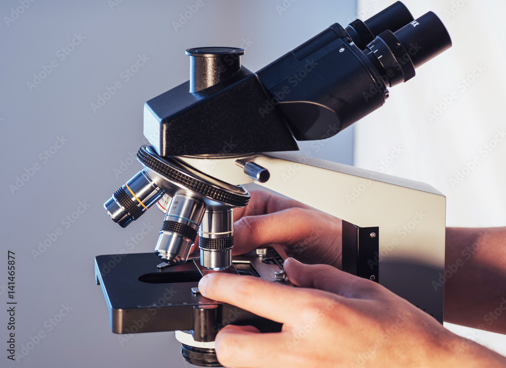 Poster close-up of scientist hands with microscope, examining samples.