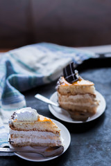 a beautiful delicious cake and the pieces in twoo white saucers beige yellow on cutting Board on dark black background close-up