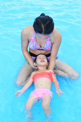 Pretty little girl with her mother in swimming pool outdoors