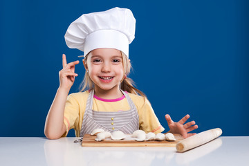 The little girl is cooking and preparing food on blue background