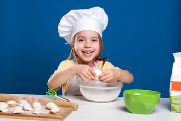 The little girl is cooking and preparing food on blue background
