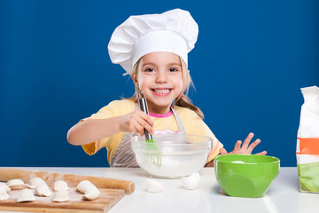 The little girl is cooking and preparing food on blue background
