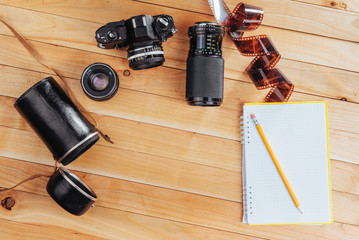 The old film camera and roll film and notebook with pencil on a wooden background