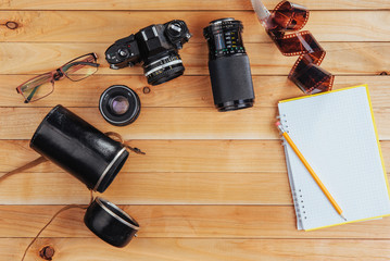 The old film camera and roll film and notebook with pencil on a wooden background