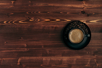 Hot coffee in black cup with crema and beans with copy space on brown old wooden board background, top view.  Rustic style.