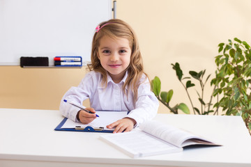 Beautiful little girl writes sitting at table