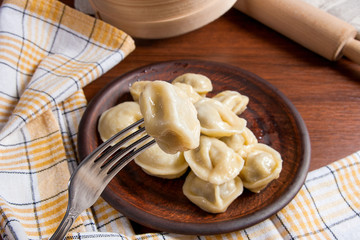 Close up view of boiled meat dumpling on metal fork. Served in clay plate Ukrainian meat dumplings or ravioli on wooden background..