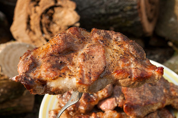 Close up view of juicy pork steak on fork cooked on an open flame grill on big white plate..