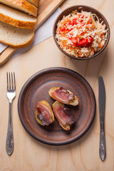 Baked potatoes with slices of bacon and eating utensils on wooden background. Sauerkraut in clay bowl and slices of white bread on cutting board..