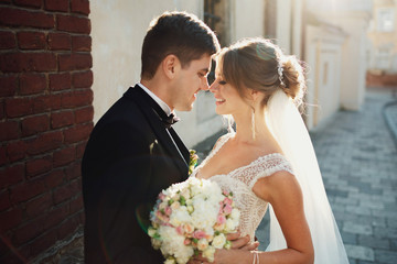 Brunette groom holds bride in lace corset tender standing with her in the rays of evening light