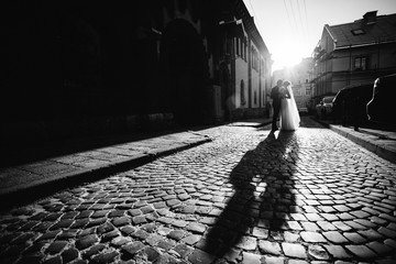 Evening sun lies long shadows of wedding couple hugging on the street