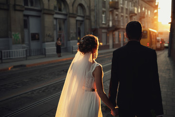 Look from behind at dreamy wedding couple walking along the tramway
