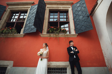 Bride and groom look in different directions standing under windows on red wall