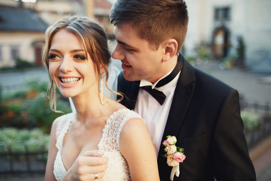 Groom hugs joyful bride from behind standing outside