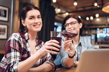 Portrait of positive woman while clinking glasses with her friend