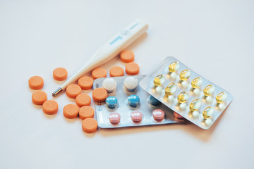 Flu. Thermometer with elevated temperature and many pills on light background