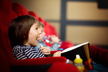 Two preschool children, twin brothers, watching movie in the cinema
