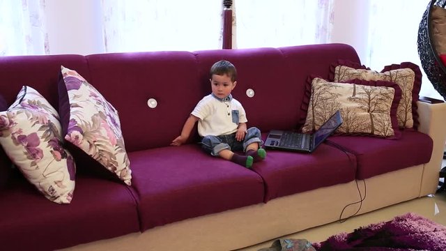 A little boy is sitting on the couch and watching TV