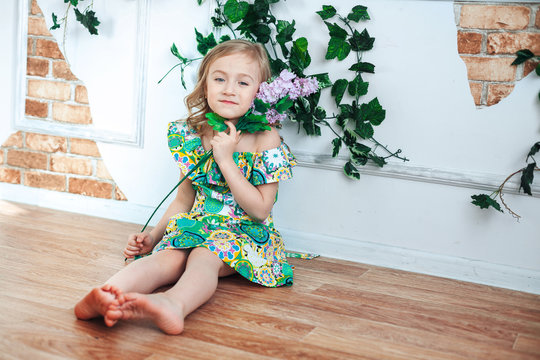 Little blond girl in a bright dress in a room decorated with flowers