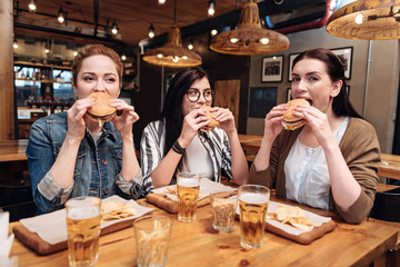 Company of delighted girls tasting burgers