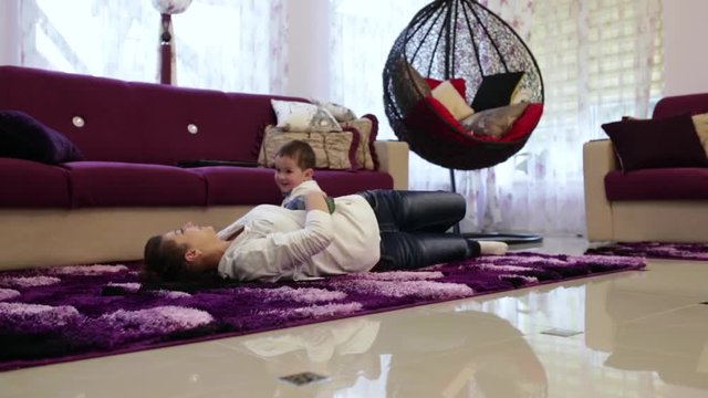 A young mother with her little son lying on the floor in the living room and watch TV. Have fun playing
