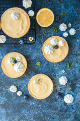 Fototapeta na wymiar Lemon curd and blueberry jam tarts with meringue and basil leaves Chamomiles whole and slices of fresh lemon on a blue rusty textured background. Copy Space. Flat lay. Top View.