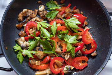 Mushrooms and fresh sweet red pepper in the pan for cooking. Spices and fresh parsley. Shallow depth of field. Toned