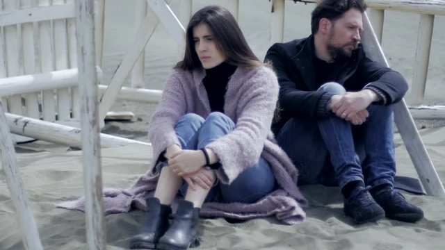 Sad angry woman looking silent boyfriend sitting on sand