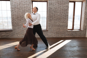 Harmonious senior dance couple dancing tango at the ballroom