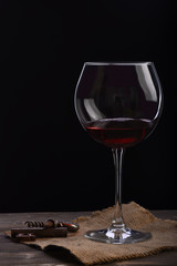 wineglass with wine, corkscrew on wooden table with sackcloth napkin