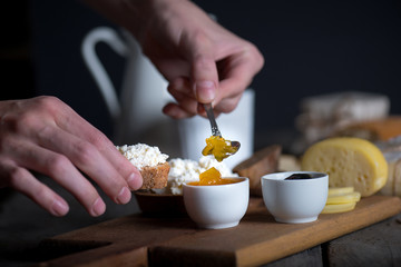 Man's hand putting jam from bowl on bread with ricotta cheese
