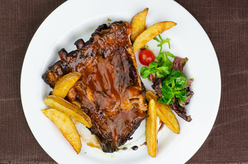 Pork Ribs With BBQ Sauce And Fried Potatoes On White Plate Shot From Above