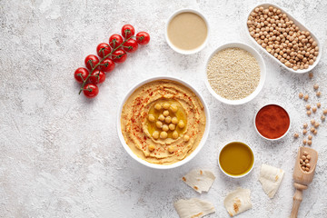 Hummus in bowl flat lay with ingridients, healthy diet natural vegetarian snack protein food. Traditional mediterranean appetizer. Sesame, paprika, tahini, pita bread and olive oil on white table