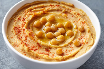 Hummus homemade traditional middle eastern dip paste close up with paprika, tahini, and olive oil, healthy diet natural vegetarian snack protein food. Traditional mediterranean appetizer on blue table