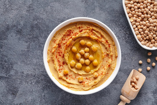 Hummus Israel dip paste close up with paprika, tahini, and olive oil, healthy diet natural vegetarian snack protein food. Traditional mediterranean appetizer on blue table