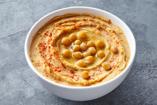 Hummus homemade middle eastern dip paste close up with paprika, tahini, and olive oil, healthy diet natural vegetarian snack protein food. Traditional mediterranean appetizer on blue table