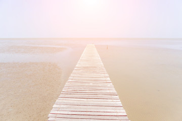 Beautiful wooden bridge extending into the sea with soft sunlight in background, traveling destination in Thailand.