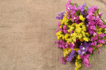 Colored dry bouquet on rustic jute background. Beautiful arrangement of flowers located on burlap vintage style useful as wallpaper
